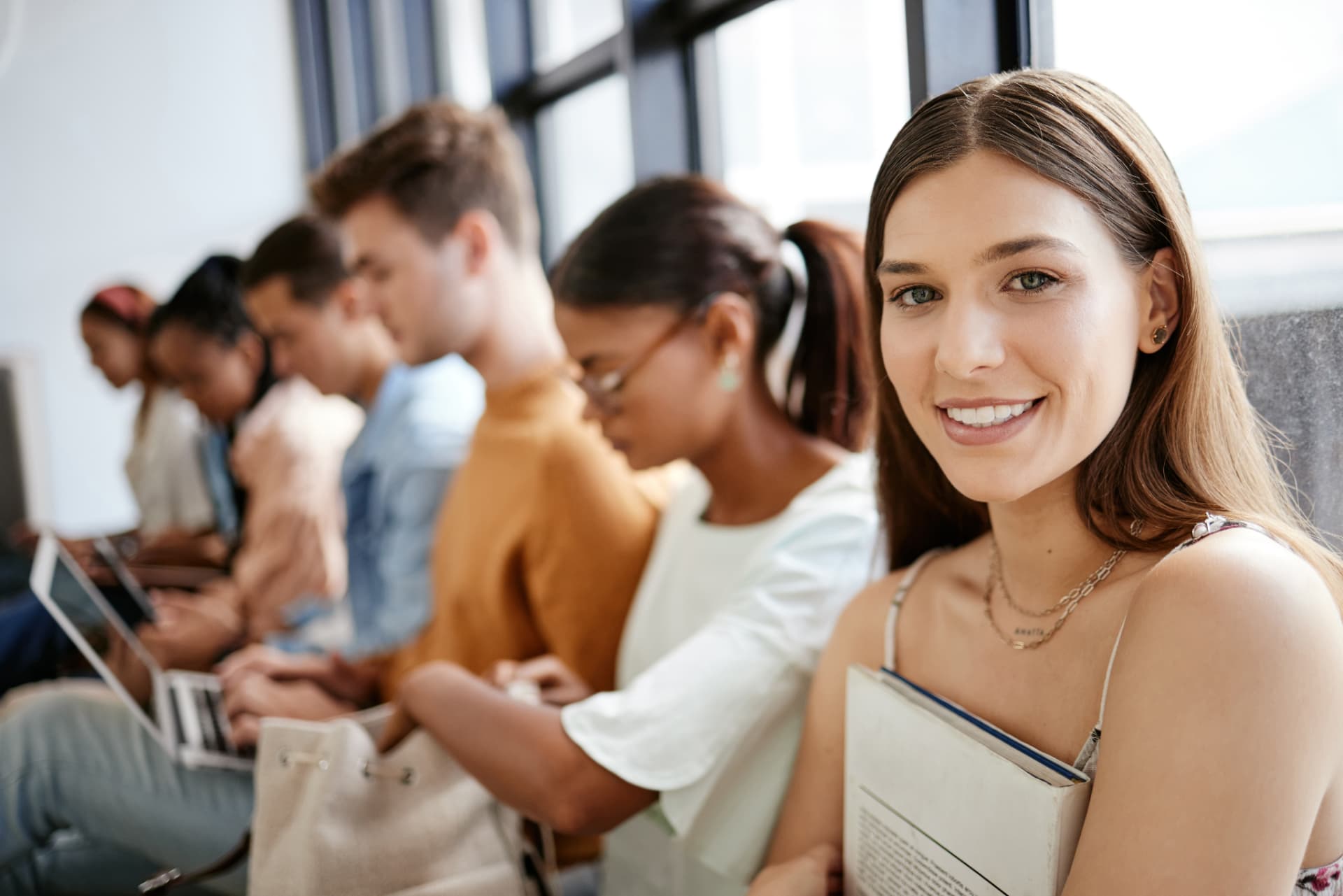Students waiting together, one smiling at the camera holding a notebook